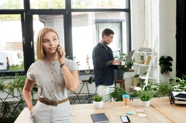 Meslektaşı son moda bir ofiste dizüstü bilgisayarıyla çalışırken genç bir kadın telefonda konuşuyor..