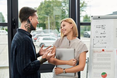İki genç profesyonel, parlak bir ofis ortamında fikir ve gülümseme paylaşıyor..
