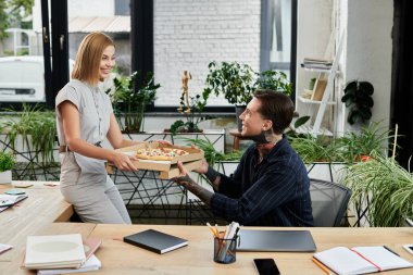 İki iş arkadaşı keyifli bir anın tadını çıkarırken biri diğerine lezzetli bir pizza sunuyor..