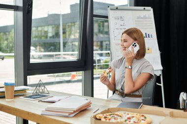 A cheerful coworker enjoys pizza and a phone call during a vibrant office break. clipart