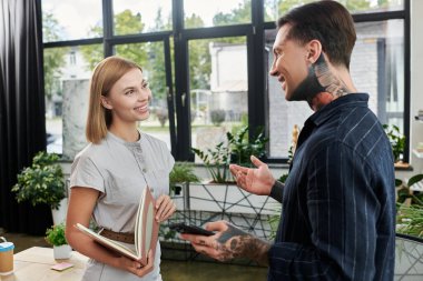 A friendly exchange unfolds between two colleagues in a bright, plant filled workspace. clipart