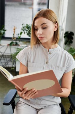 A focused young coworker immerses herself in a book while seated at her workspace. clipart