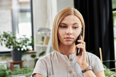 Genç bir profesyonel, çevresi yeşilliklerle çevrili telefonuyla odaklanmış bir konuşma yapıyor..