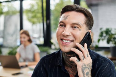 Genç bir iş arkadaşı, modern ofis ortamında gülümserken canlı bir telefon görüşmesi yapmaktan zevk alır..