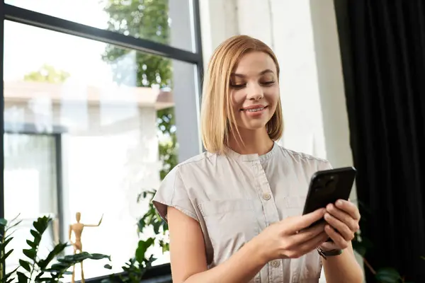 stock image Young woman holding phone in office.