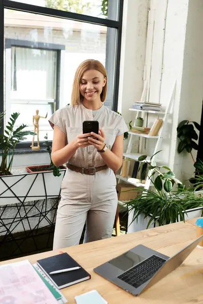 Genç bir profesyonel, canlı bir ofiste dururken akıllı telefonuyla vakit geçirmekten zevk alır..