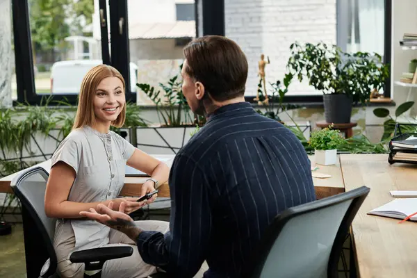 stock image Two coworkers engage in a lively discussion while surrounded by vibrant office plants.