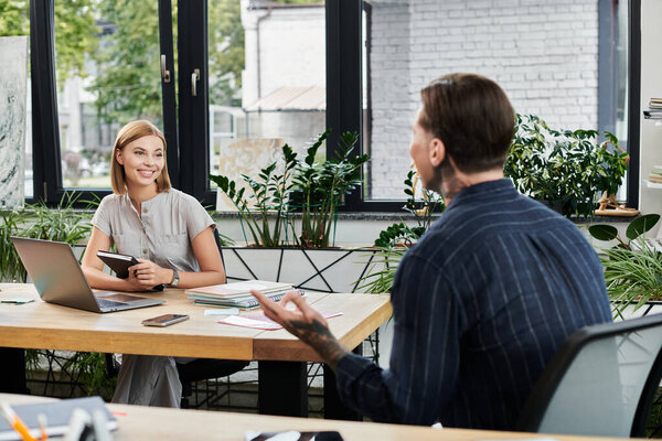 Два молодых специалиста делятся идеями и сотрудничают в ярком, заполненном растениями рабочем пространстве.