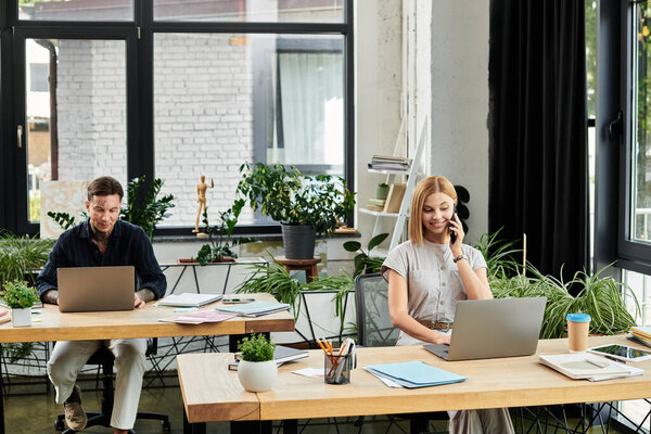 Два сотрудника выполняют задания за своими рабочими столами, сосредоточены и окружены зеленью.