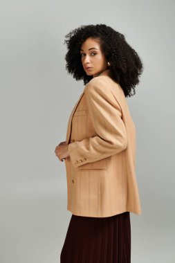 Şık bir kadın şık kıyafetini sergilerken yumuşak ışıkta kendine güvenen bir poz veriyor..