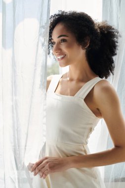 Şık bir kadın pencerenin kenarında duruyor, sıcak güneş ışığının tadını çıkarırken gününü düşünüyor..