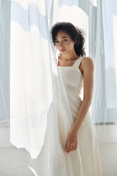 A fashionable woman in chic attire enjoys the soft light filtered through delicate curtains.