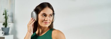 Neşeli bir ifadeyle genç esmer bir kadın evde dinlenirken, sıcaklık ve rahatlıkla müzik dinler..