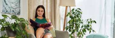 A young brunette woman with short stature relaxes in her living room, deeply engaged in a magazine amidst vibrant indoor plants. clipart