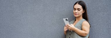 Kısa boylu esmer bir kadın açık havada, akıllı telefonuyla meşgul, merakla çevresini keşfediyor..