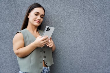 Neşeli esmer bir kadın duvarın karşısında duruyor, dışarıda güzel, aydınlık bir günde akıllı telefonuyla meşgul oluyor..