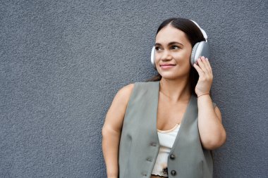 Neşeli esmer bir kadın neşeli bir gülümsemeyle açık havada müzik dinliyor, güneşin altında güneşleniyor..