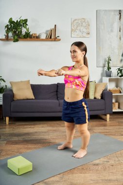 Azimli, kısa boylu, esmer bir kadın evinde çalışıyor, rahat yaşam alanının keyfini çıkarırken, spor yapmaya odaklanıyor..