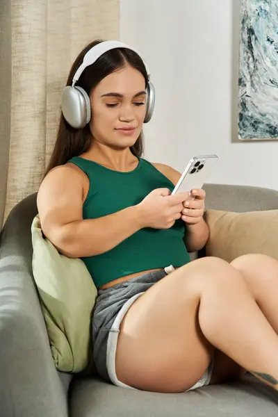 stock image A short-statured woman relaxes on a couch, fully immersed in music through her headphones, enjoying her cozy space.