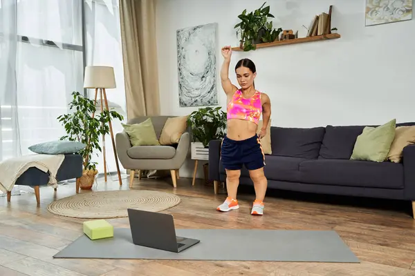 stock image A young brunette woman with a short stature exercises at home, following an online workout, showcasing her dedication and energy.