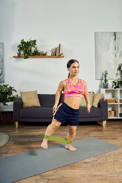 stock image A dedicated young woman engages in a workout routine at home, focusing on her fitness while using resistance bands.