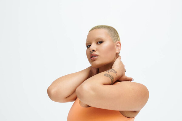 A young woman with a shaved head poses with grace, celebrating her vibrant fashion choice.
