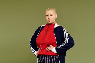 Kendine güvenen genç kel bir kadın canlı giyinmiş yeşil bir arka plana karşı tavır takınıyor..