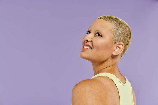 A young bald woman in vibrant attire turns happily, showcasing her unique fashion sense.