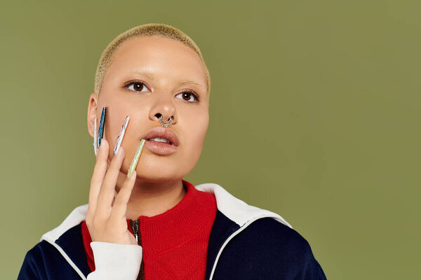 A young woman flaunts her vibrant style and artistic nails against a green backdrop.