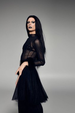 Çarpıcı bir travesti, dikkat çekmeden şık bir siyah elbisenin içinde cesur bir görünüm sergiliyor..