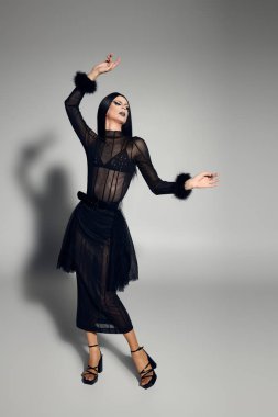 Moda kraliçesi, stüdyoda kendine güvenen bir poz verirken göz kamaştırıcı bir siyah elbise sergiliyor..