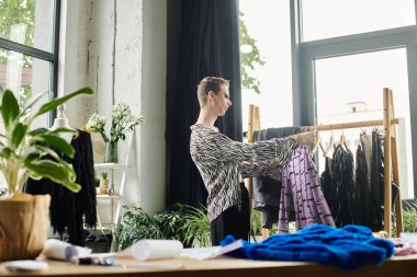 Cinsiyet akışkan bir moda tasarımcısı verimli bitkilerle dolu parlak bir stüdyo dairesinden canlı kumaşlar seçer..