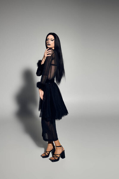 Эта модная королева драга демонстрирует элегантный черный наряд, излучающий уверенность в творческой обстановке студии.