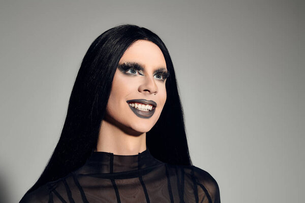 This stylish individual radiates confidence in a sleek black outfit against a grey backdrop, exuding elegance.