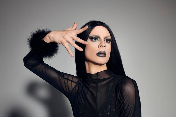 A captivating drag performer showcases their bold fashion sense in a sleek black outfit with dramatic flair.