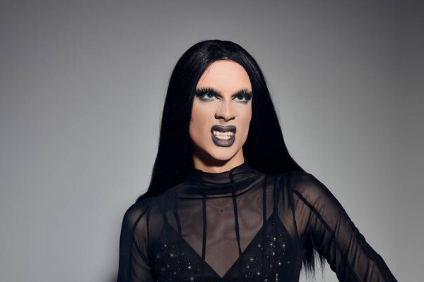 The fashionable drag queen poses confidently in a sleek black ensemble against a neutral background, exuding artistry.