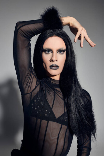 A fashionable drag queen exudes confidence in a sleek black ensemble while striking a dramatic pose.