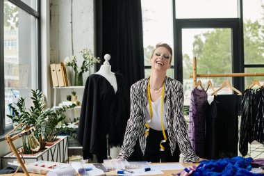 Cinsiyet değiştiren bir moda tasarımcısı ilham dolu, parlak, havadar bir stüdyoda tasarımlar üzerinde çalışırken güler..
