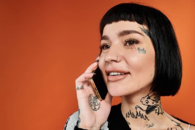 Çarpıcı dövmeleri ve kısa saçı olan genç bir kadın eğlenceli bir telefon görüşmesinden hoşlanıyor.