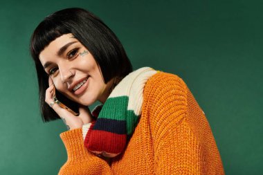 Kısa saçlı ve dövmeli genç bir kadın neşeli pozlar veriyor, sıcak süveterini ve neşeli ifadesini sergiliyor.