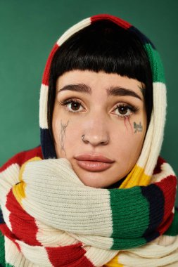 A young woman with short hair and tattoos embraces a warm sweater and scarf, in a studio. clipart