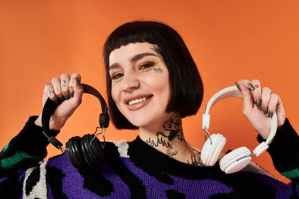 Уверенная молодая женщина демонстрирует модные наушники, в то время как носит красочный свитер в студии.