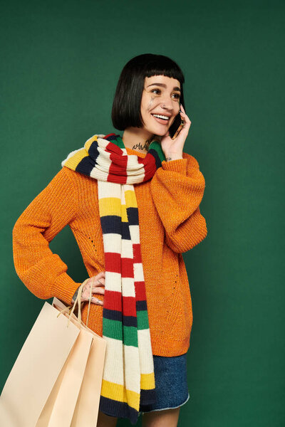 Татуированная молодая женщина улыбается по телефону, тепло одетая на ярком зеленом фоне.