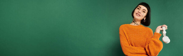 A young woman with tattoos confidently poses in a cozy sweater, showcasing her unique style in a vibrant studio.