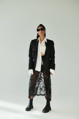 Şık giyinmiş, kendine güvenen genç bir kadın, ışıl ışıl bir moda havası yayıyor..