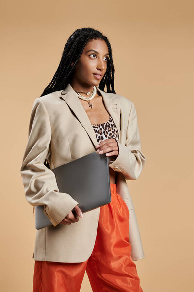 Молодая женщина излучает уверенность в модном наряде, держа в руках ноутбук, готовый к приключениям.