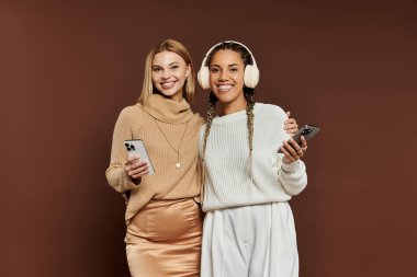 A cheerful couple in stylish autumn outfits shares a laugh while using their phones. clipart