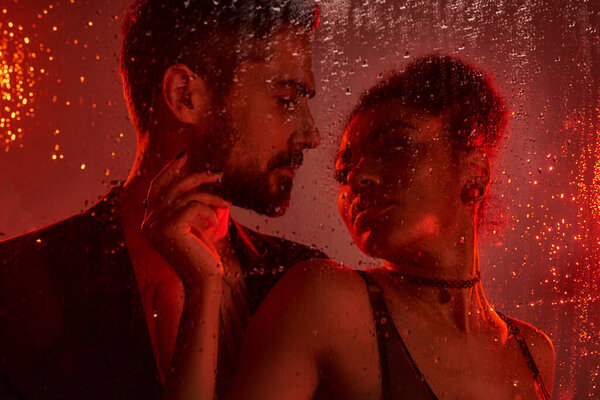 Любящая пара разделяет интимный момент, обрамленный каплями дождя и мягким, романтическим освещением.