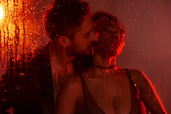 Пара разделяет нежный поцелуй, окруженный теплым светом, в то время как капли дождя каскадом вокруг них.