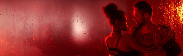 Любящая пара разделяет интимный момент, завернутый в руки друг друга, светящийся в красном свете.